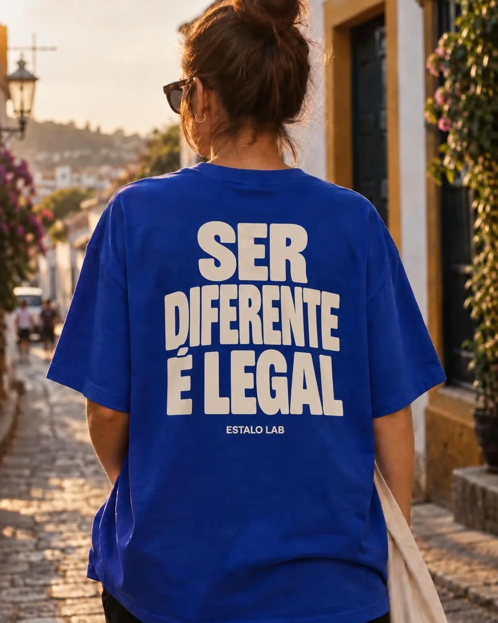Pessoa de costas numa rua de pedra, vestindo a camiseta azul com SER DIFERENTE É LEGAL em letras creme